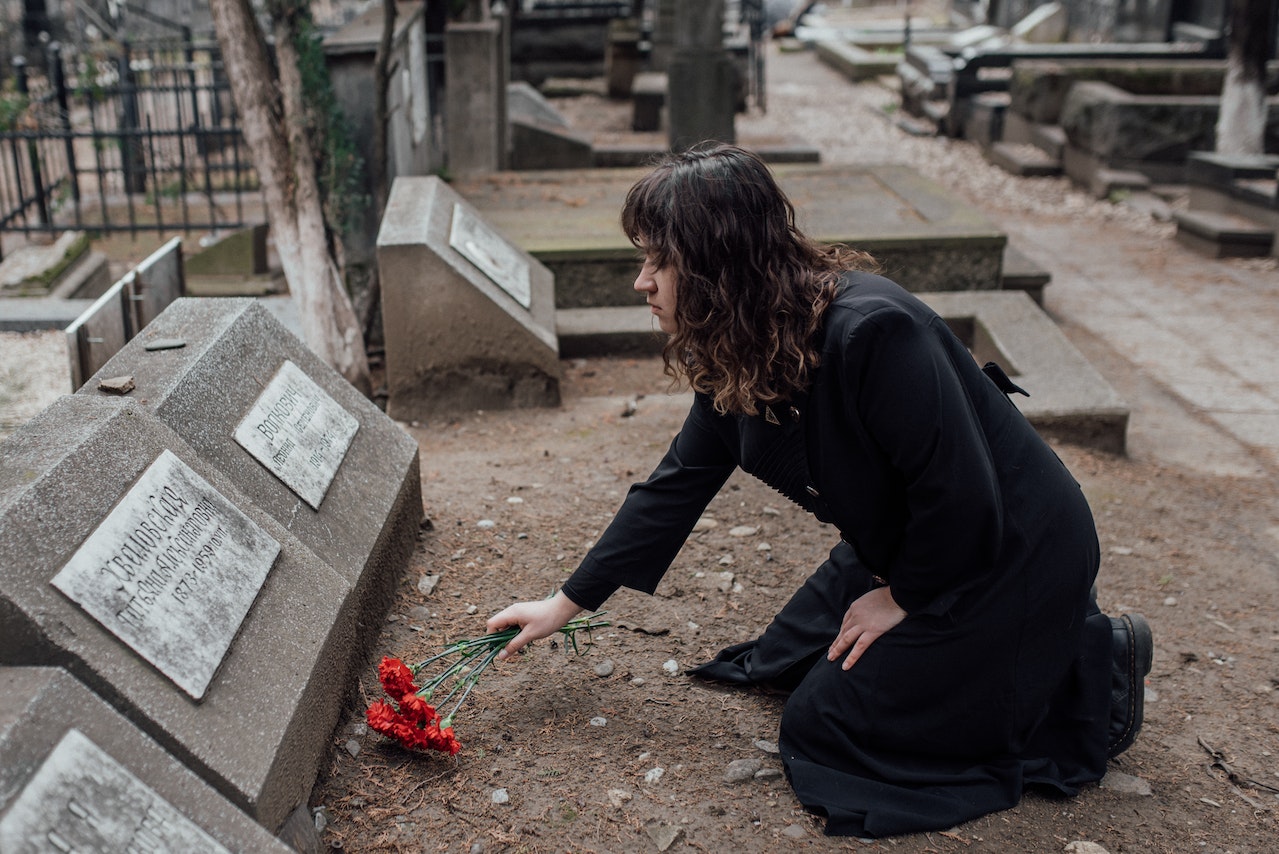 Kobieta ubrana na czarno kładzie czerwone kwiaty na grobie bliskiej osoby