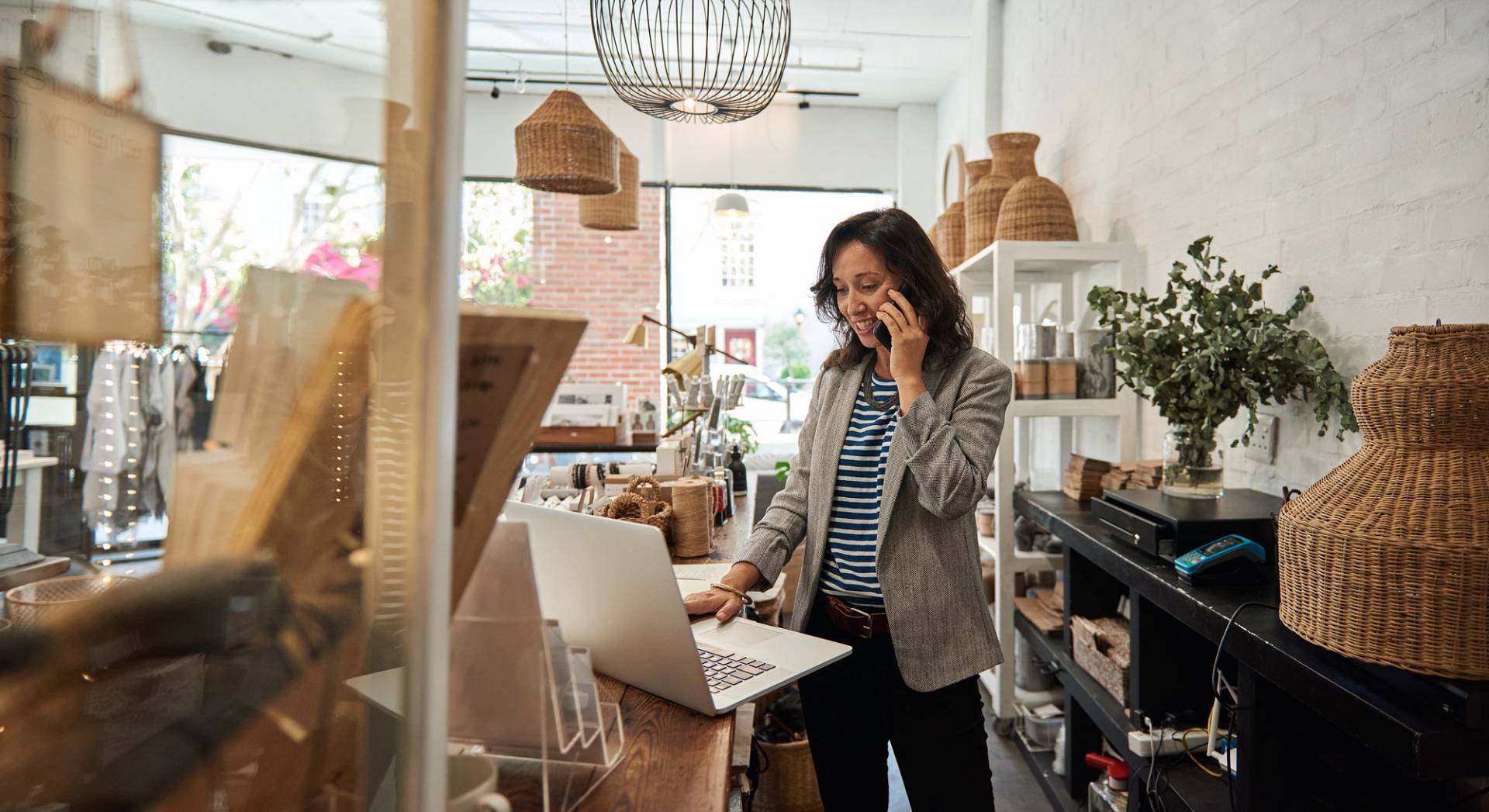 Kobieta pracuje w sklepie wielobranżowym i rozmawia przez telefon patrząc w laptopa