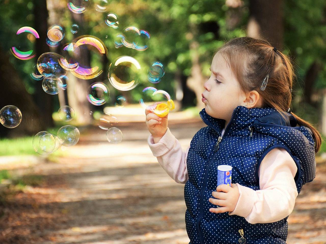 Dziewczynka puszcza bańki mydlane na spacerze w parku