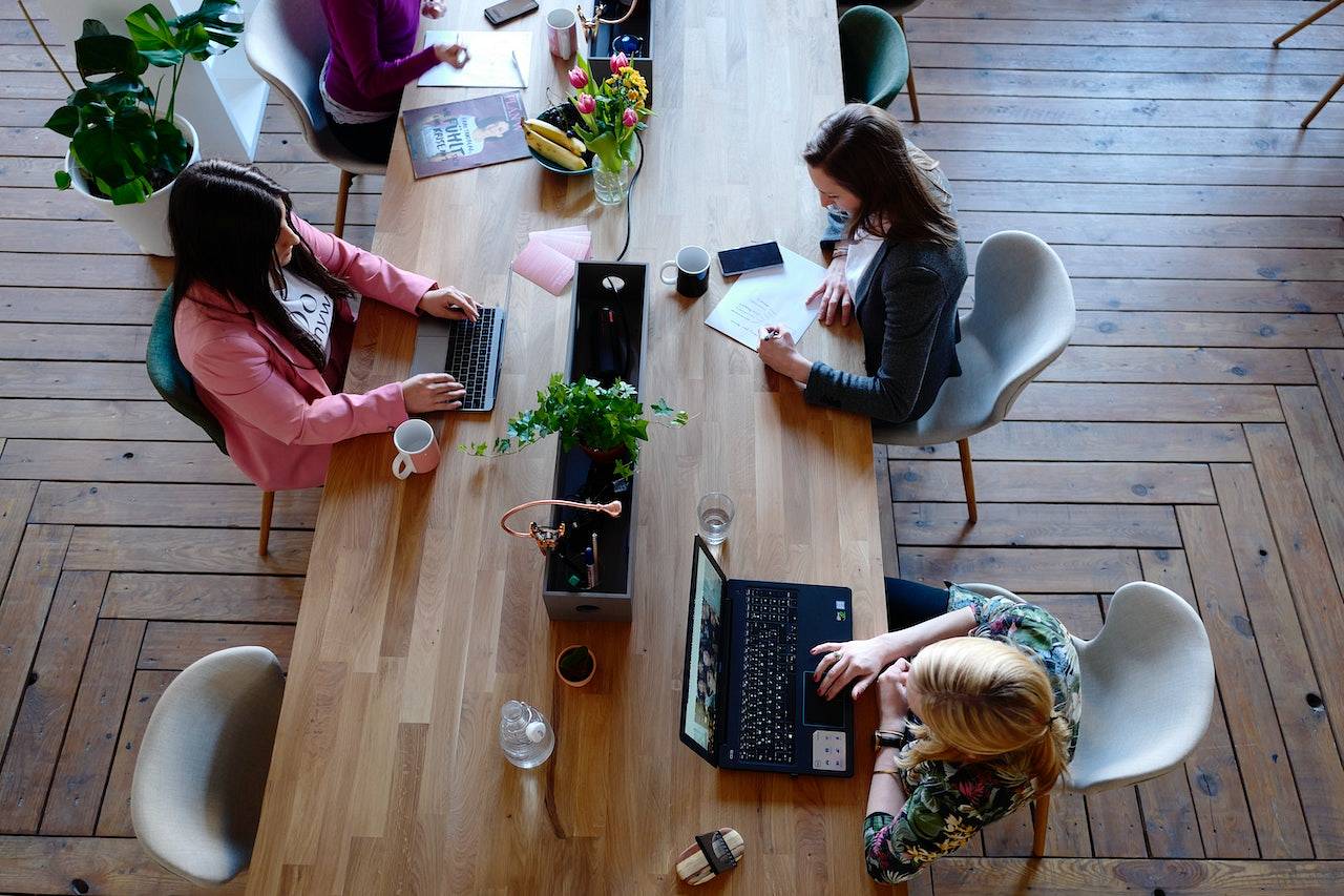 Kilka osób siedzi w biurze przy jednym, długim stole i pracuje